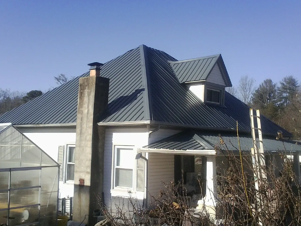 Dark blue standing seam metal roof on a white farmhouse with dormer — Slate & Tile Roof Repair by Roofing Brothers in Osyka