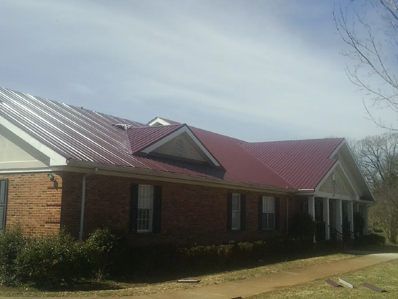 Red metal roof with gabled entries on a long brick building, from a Hail Damage Roof Repair job in Osyka