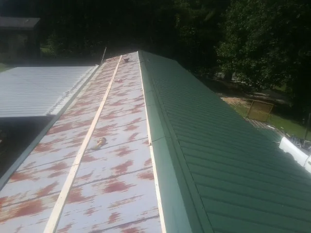 Old rusted panels beside newly installed green metal roofing — Wind Damage Roof Repair by Roofing Brothers in Osyka