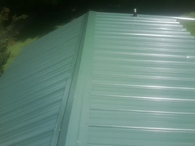 New green metal panels meeting at the ridge of a roof — Flat Roof Repair work by our crew in Osyka