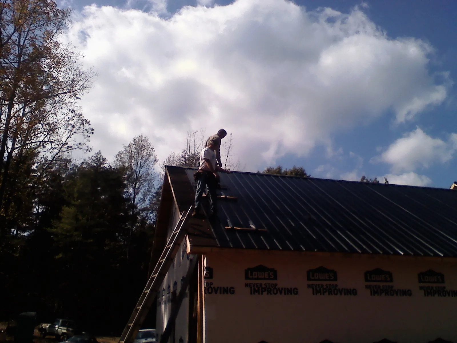 Roofer fastening dark metal panels high against a cloudy sky, from a Roof Inspection job in Osyka