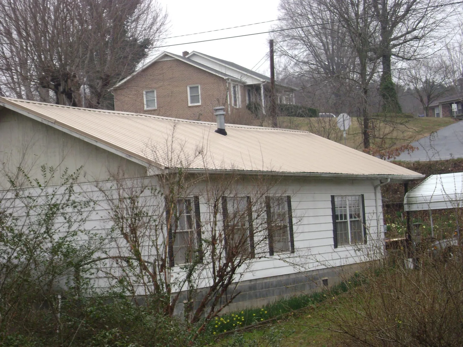 Tan metal roof on a white sided house set into a hillside — Commercial Roofing by Roofing Brothers in Osyka