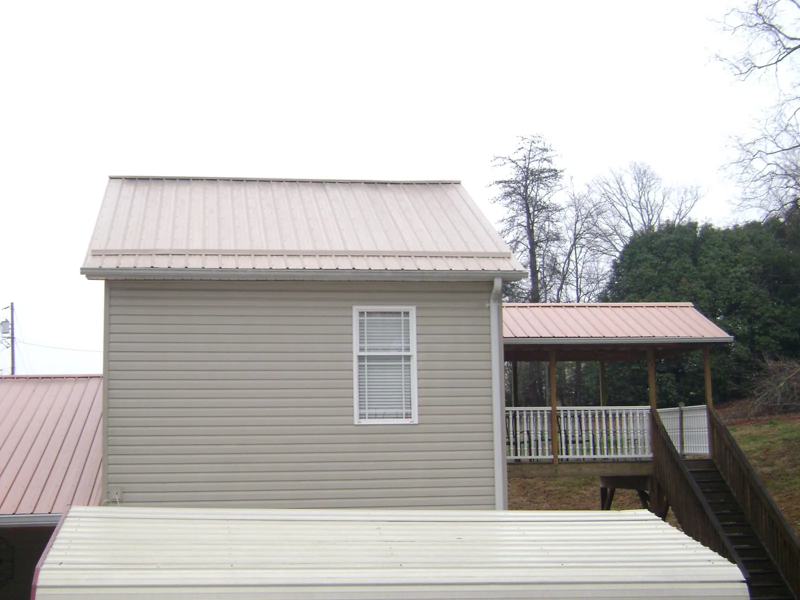 Tan metal roofs on a two story addition and attached porch, from a Roof Replacement job in Osyka